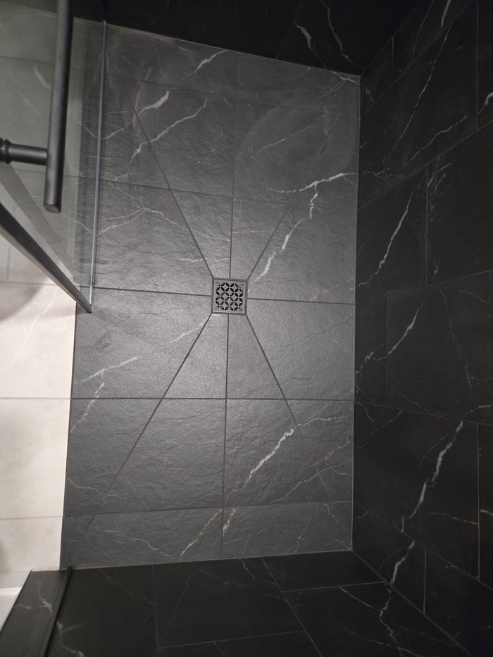 Shower pan pitched to a centre drain in dark marble-look tile
