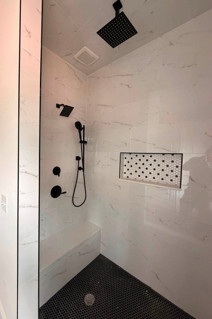 Marble-look shower with black penny floor, bench and niche